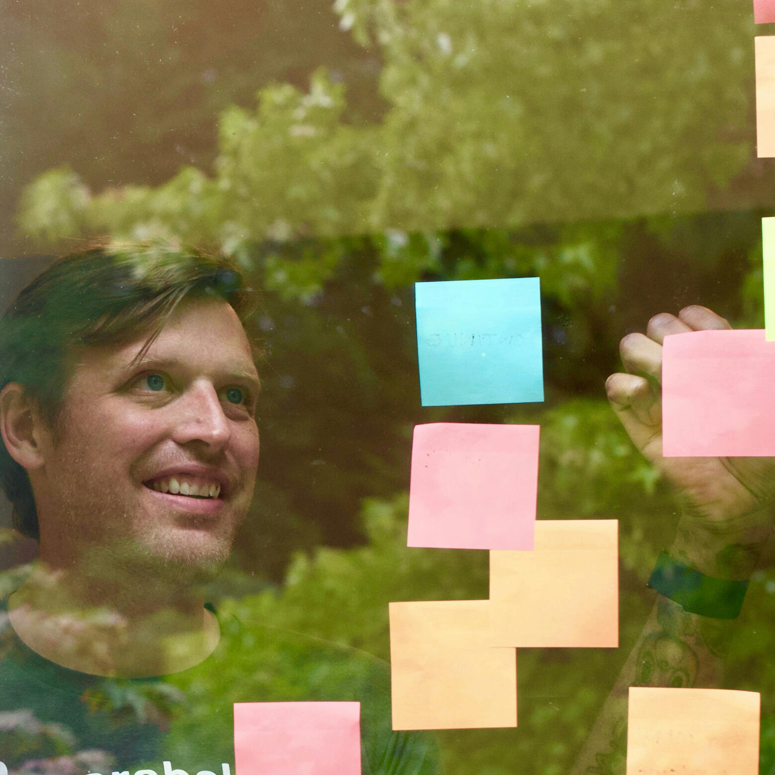 A man smiling and looking at Post-its on a window